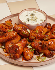 A plate of saucy chicken wings garnished with green onions, served with a bowl of blue cheese dip on a tiled surface.
