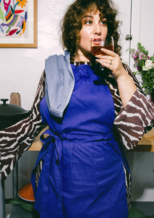 A chef wearing a blue Hosting Apron sips wine from a glass