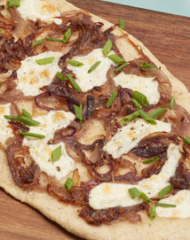 Flatbread topped with caramelized onions, melted cheese, and chopped green onions on a wooden surface.