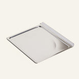 A rectangular stainless steel tray with a raised edge on one side, placed on a light background.