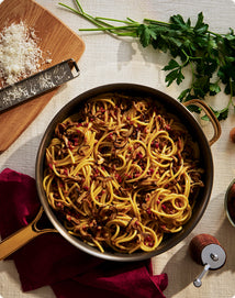 Pasta dish in a pan with herbs and Parmesan cheese on a table