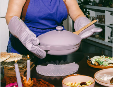 A chef wearing a blue Hosting Apron serves a meal in a purple Always Pan