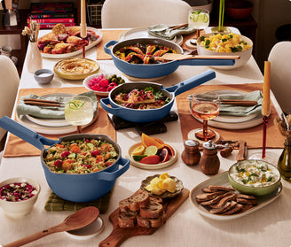 Dining table set with blue cookware, plates of food, and glasses on a neutral background