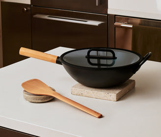 Black wok with wooden handle and spatula on a kitchen counter