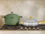 Green ceramic pot and silver pan with gold handles on a stove.