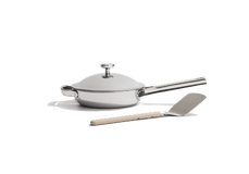 A stainless steel frying pan with a lid and a metal spatula with a beige handle on a white background.