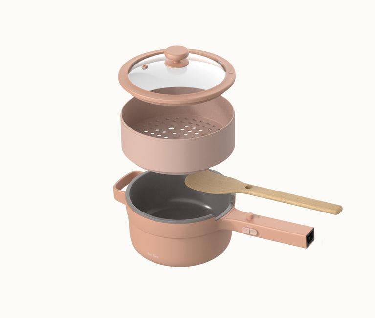 A pink cooking pot with a lid, a steamer insert, and a wooden spoon resting across the top, all displayed on a white background.