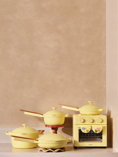Set of yellow cookware including pots and a small stove on a neutral background