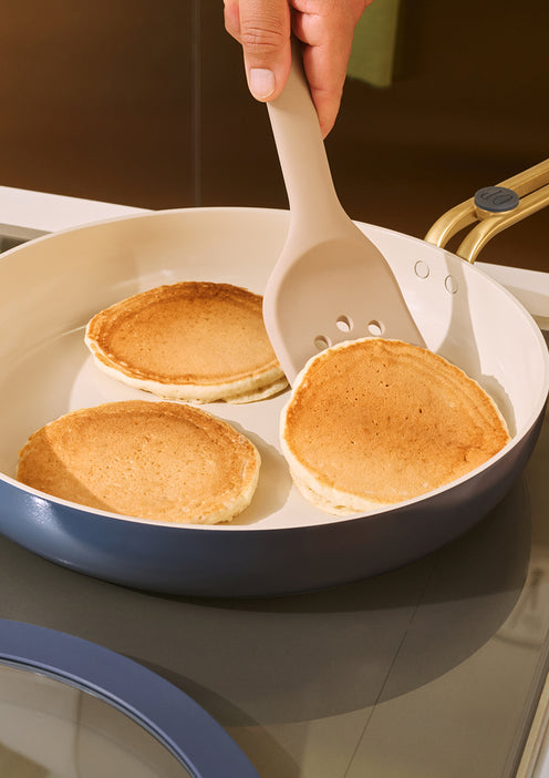 Person flipping pancakes in a pan with a spatula