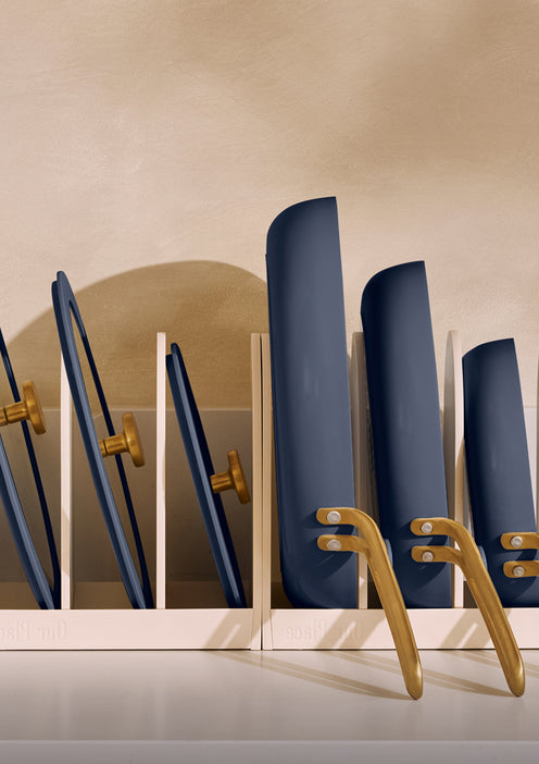 Set of blue pans in a gold holder against a beige wall.