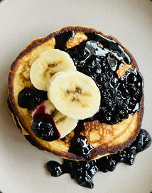 A stack of pancakes topped with banana slices and blueberry sauce sits on a light-colored plate.