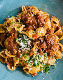 A plate of orecchiette pasta topped with a chunky meat tomato sauce, grated cheese, and chopped parsley on a blue dish.