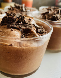 Close-up of glass cups filled with chocolate mousse, topped with chocolate shavings, set on a white surface.