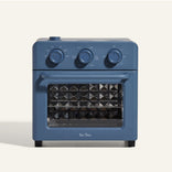 A blue countertop oven with three control knobs and a glass door, displaying the brand name Our Place at the bottom.