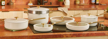 Set of white cookware with gold handles on a wooden kitchen counter.
