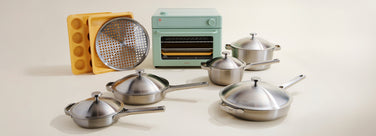 Set of stainless steel cookware with a retro-style oven and toaster on a light background
