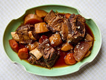 A plate of braised short ribs served with chunks of carrots, potatoes, and turnips in a brown sauce on a light green oval dish.