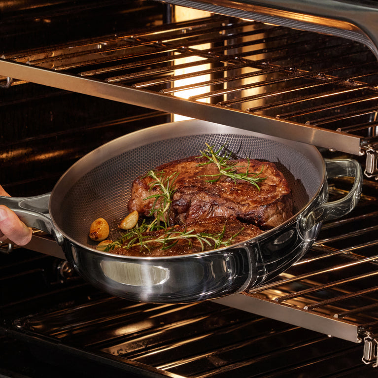 A person places a pan with cooked steak, garlic, and rosemary into an open oven.