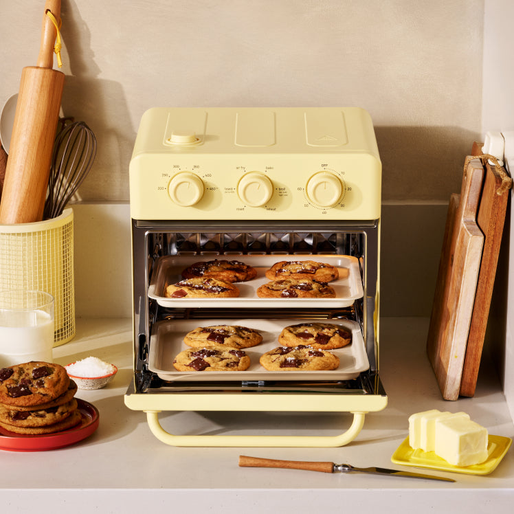 Yellow toaster oven with cookies on trays in a kitchen setting