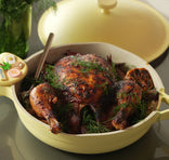 Roasted chicken in a yellow ceramic dish on a reflective surface