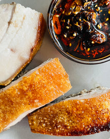 Slices of roasted pork belly with a side of spicy sauce on a light surface