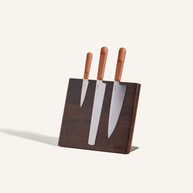 Three kitchen knives with brown handles are placed in a dark wooden knife block against a light background.