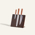 Three kitchen knives with brown handles are placed in a dark wooden knife block against a light background.