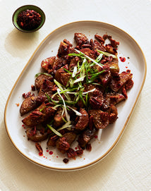 Plated dish of cooked meat with green onions on a white surface