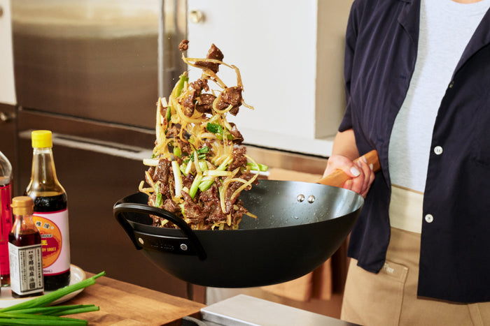 A hand holding a wok and tossing food inside