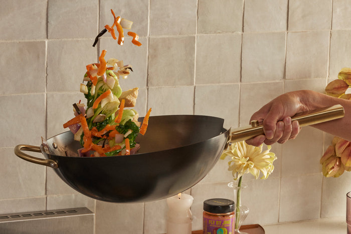 A hand holding a wok with food cooking inside of it