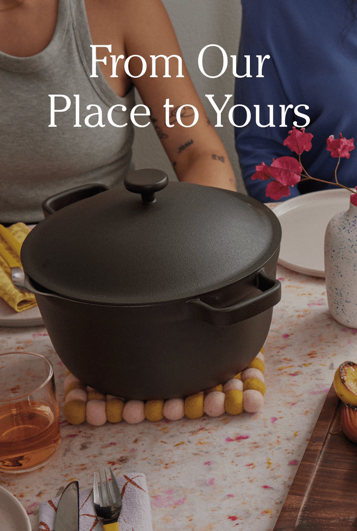 Translation missing: en.A black Dutch oven sits on a trivet at a set dining table with flowers, dishes, and drinks; text reads From Our Place to Yours