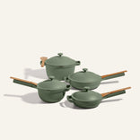 The Cookware Set features four matte green pots and pans with matching lids and wooden handles, artfully arranged on a neutral background—ideal for fans of the Always Pan or Perfect Pot.