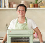 Person wearing a green apron holding a green appliance in a kitchen setting.