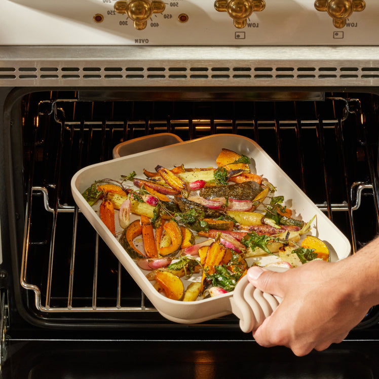 A beige Mini Griddle Pan with roasted vegetables is removed from the oven