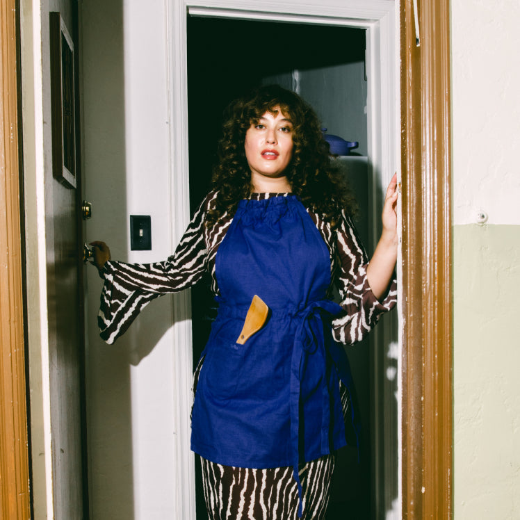 A chef wears a blue Hosting Apron with a spatula in the pocket