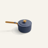 A blue saucepan with a lid and a wooden handle, placed on a light-colored surface.