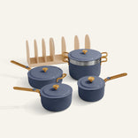 A set of four blue Essentials Saucepan Set pots and pans with wooden handles and lids, featuring a non-toxic nonstick finish, next to a beige vertical rack organizer on a light background.