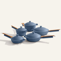 The Cookware Set+ features five blue nonstick ceramic pieces with wooden handles and lids, including assorted pots and pans, beautifully arranged on a light background.