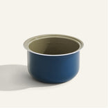 A blue and beige round cooking pot insert with measurement markings on the inside, placed on a light background.