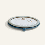 A round, flat, white and blue plastic kitchen lid with a vent and steam release valve, photographed on a plain light background.