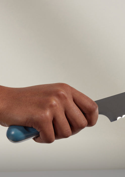 A hand firmly gripping the blue handle of a large kitchen knife against a plain background.