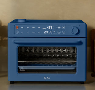 A blue countertop air fryer oven with digital controls displays 425°F and a timer set to 24:59. The oven door is closed, showing an empty cooking rack inside.