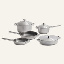 The Titanium Pro Cookware Set + Braiser features five pieces crafted from stainless steel: two saucepans with lids, a stockpot with lid, a sauté pan with lid, and a frying pan—all elegantly arranged on a plain background.