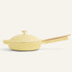 A pale yellow sauté pan with a matching lid and a long wooden handle, shown on a clean off-white background.
