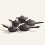 Cookware Set+ features five black ceramic nonstick pieces with wooden handles and matching lids, elegantly arranged on a light background—ideal for modern kitchens.