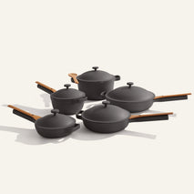 Cookware Set+ features five black ceramic nonstick pieces with wooden handles and matching lids, elegantly arranged on a light background—ideal for modern kitchens.
