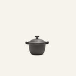 The Petite Perfect Pot, matte black with a lid and side handles, is centered on a plain off-white background.