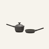The Tiny Cookware Duo, featuring a black saucepan with lid and a matching frying pan, is displayed side by side on a light background.