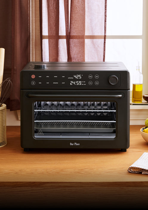 A black Our Place countertop oven on a wooden counter with a digital display reading 425 degrees.