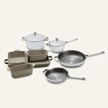 A Titanium Pro Cookware + Bakeware Set (2.0) consisting of two stainless steel lidded pots and two frying pans, alongside several tan ceramic bakeware dishes stacked on a rectangular tray.